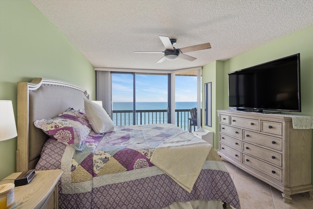 tiled bedroom featuring access to exterior, a textured ceiling, expansive windows, and ceiling fan