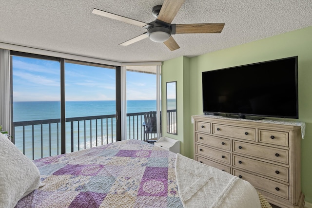 bedroom with ceiling fan, expansive windows, a textured ceiling, access to outside, and a water view