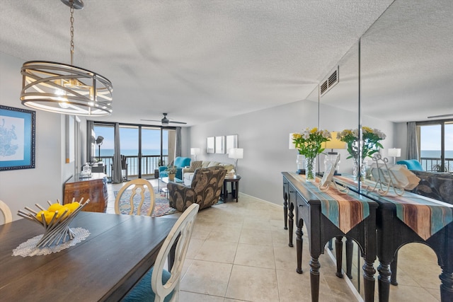 tiled dining room featuring vaulted ceiling, ceiling fan with notable chandelier, a water view, and a textured ceiling