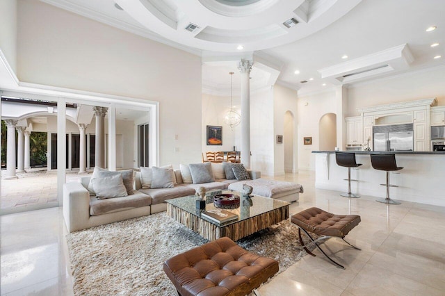 tiled living room with a towering ceiling, decorative columns, ornamental molding, and a notable chandelier