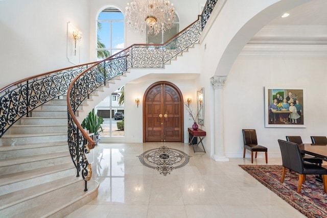 foyer with a chandelier, a towering ceiling, crown molding, and decorative columns