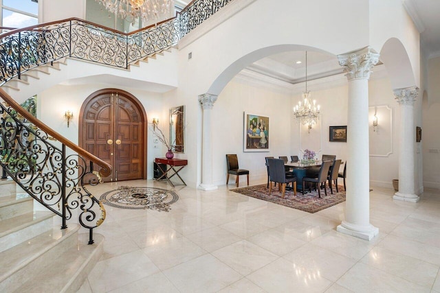 entrance foyer with a notable chandelier, a towering ceiling, ornamental molding, and ornate columns