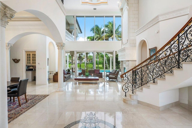 entryway with a high ceiling, decorative columns, plenty of natural light, and ornamental molding