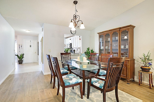 dining room with light hardwood / wood-style floors, vaulted ceiling, and an inviting chandelier