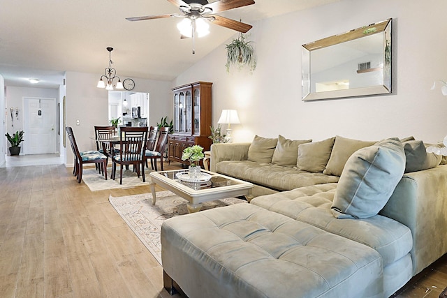 living room with ceiling fan with notable chandelier, vaulted ceiling, and light hardwood / wood-style flooring