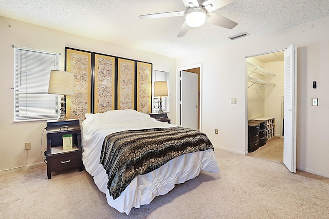 bedroom featuring ceiling fan, a spacious closet, a textured ceiling, light carpet, and a closet