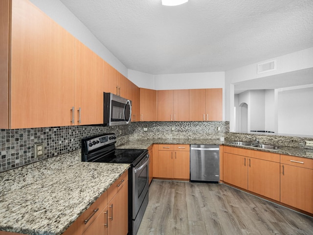 kitchen with sink, tasteful backsplash, light stone counters, appliances with stainless steel finishes, and light wood-type flooring