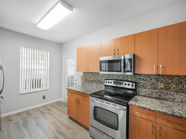 kitchen featuring stone counters, stainless steel appliances, a textured ceiling, decorative backsplash, and light wood-type flooring