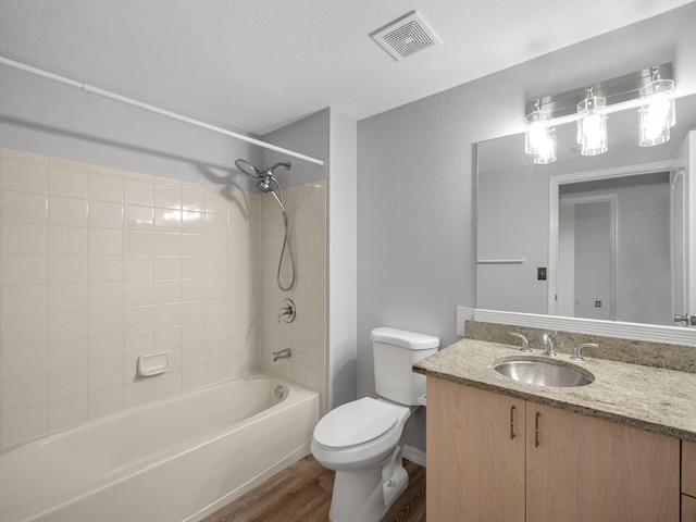 full bathroom featuring tiled shower / bath combo, wood-type flooring, a textured ceiling, toilet, and vanity