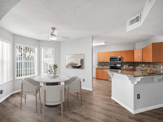 kitchen with stainless steel appliances, tasteful backsplash, dark stone countertops, a textured ceiling, and hardwood / wood-style flooring