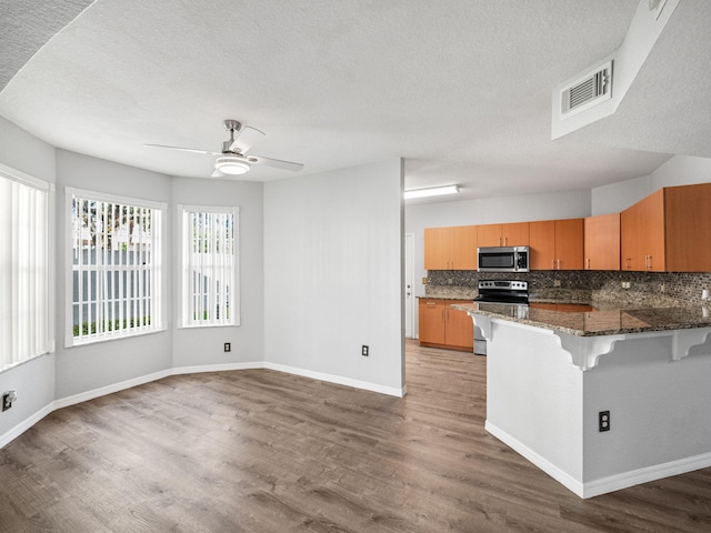 kitchen featuring hardwood / wood-style floors, backsplash, a kitchen breakfast bar, kitchen peninsula, and stainless steel appliances