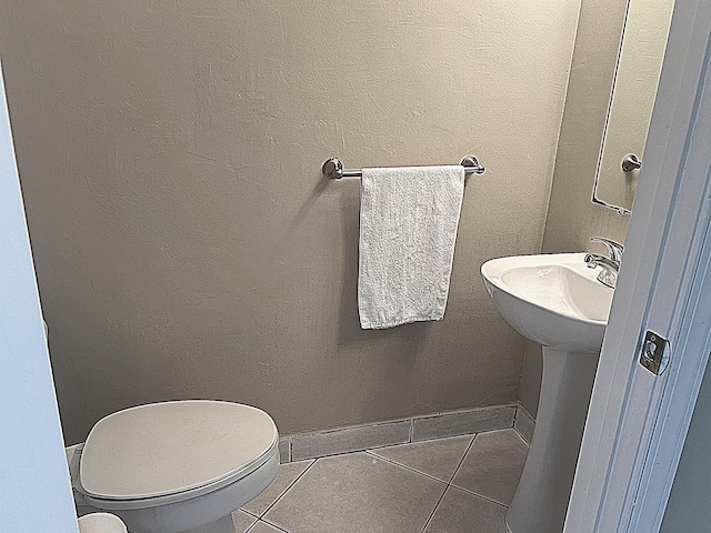 bathroom featuring tile patterned floors, baseboards, toilet, and a sink