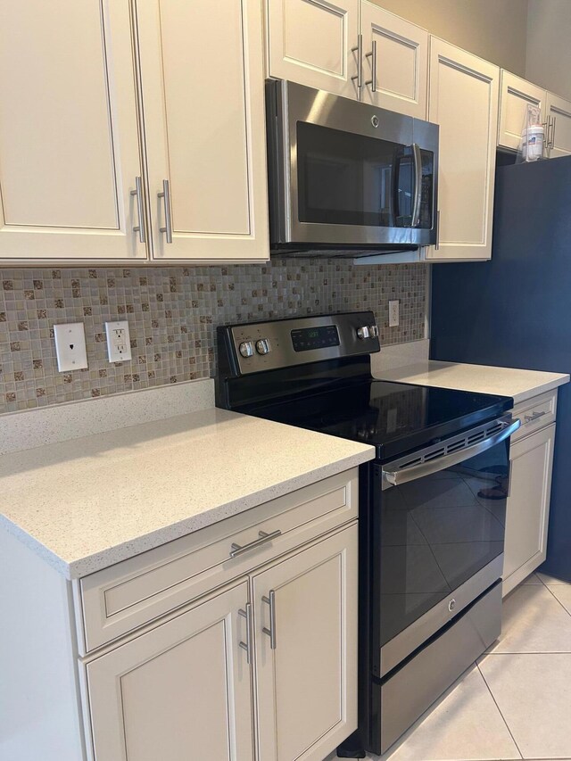 kitchen featuring light tile patterned floors, light stone countertops, stainless steel appliances, white cabinetry, and backsplash