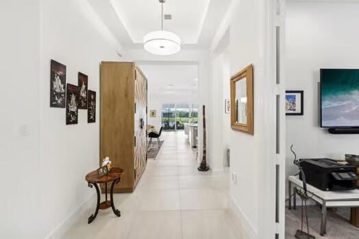 hall with a raised ceiling and light tile patterned floors