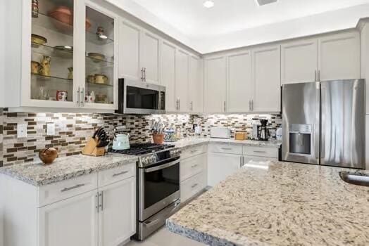 kitchen with light stone countertops, appliances with stainless steel finishes, backsplash, and white cabinetry