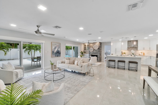 tiled living room featuring a stone fireplace and ceiling fan