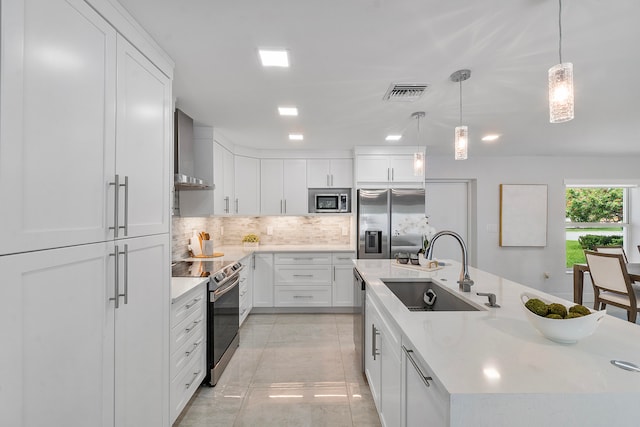 kitchen featuring sink, wall chimney range hood, built in appliances, decorative light fixtures, and white cabinets