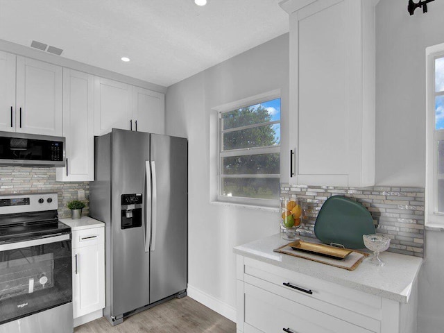 kitchen featuring decorative backsplash, light stone countertops, stainless steel appliances, light hardwood / wood-style floors, and white cabinetry