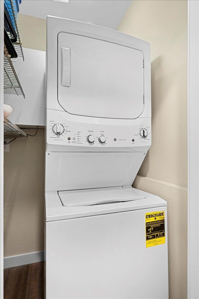 clothes washing area with dark hardwood / wood-style flooring and stacked washer / drying machine