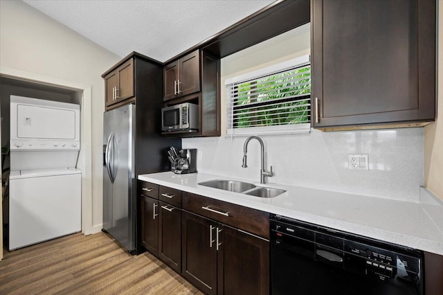 kitchen featuring stacked washing maching and dryer, dark brown cabinetry, stainless steel appliances, sink, and light hardwood / wood-style flooring