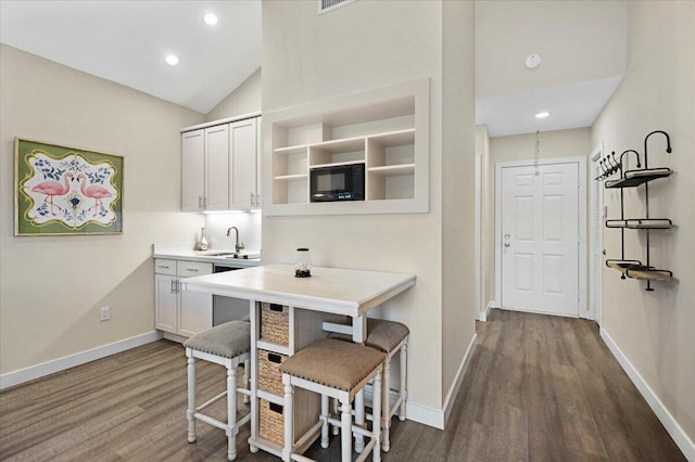 kitchen with black microwave, sink, vaulted ceiling, white cabinets, and hardwood / wood-style flooring