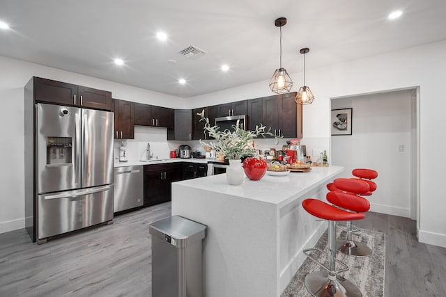 kitchen featuring kitchen peninsula, appliances with stainless steel finishes, dark brown cabinetry, light hardwood / wood-style floors, and a breakfast bar area