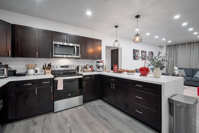 kitchen with kitchen peninsula, appliances with stainless steel finishes, dark brown cabinets, pendant lighting, and light hardwood / wood-style flooring