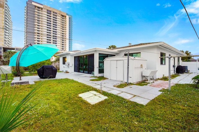 rear view of property with a yard, a patio, a storage unit, and a sunroom