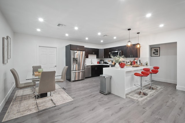 kitchen with appliances with stainless steel finishes, dark brown cabinetry, light hardwood / wood-style flooring, hanging light fixtures, and a breakfast bar area