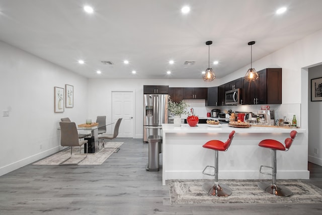 kitchen with appliances with stainless steel finishes, a breakfast bar, dark brown cabinetry, pendant lighting, and light hardwood / wood-style floors