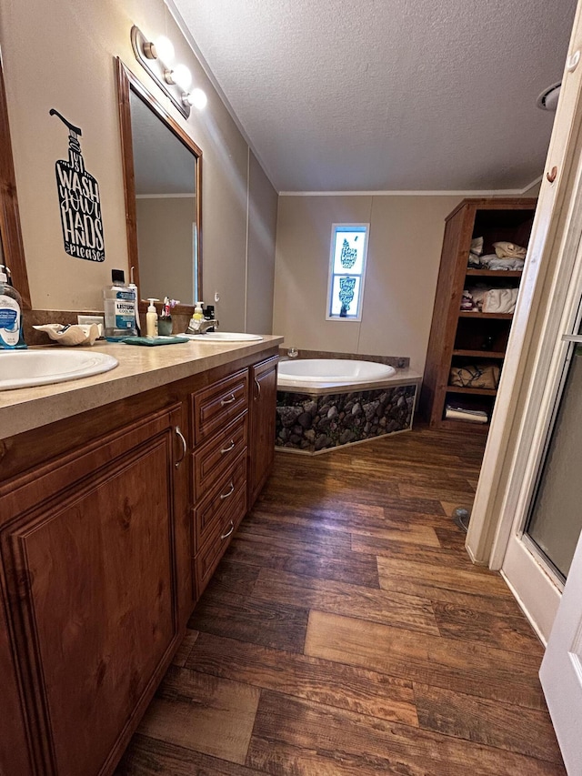 bathroom with hardwood / wood-style floors, ornamental molding, vanity, a washtub, and a textured ceiling