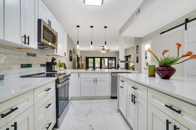 kitchen featuring pendant lighting, ceiling fan, a barn door, white cabinetry, and stainless steel appliances