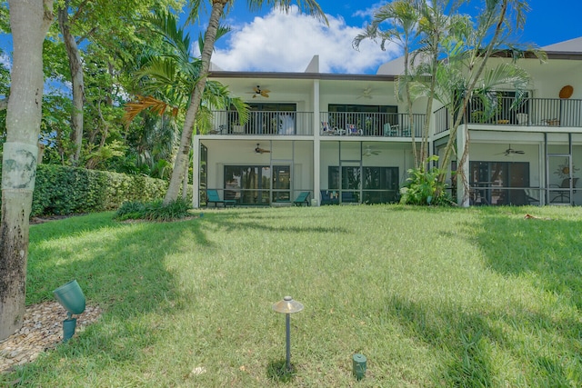 back of property with ceiling fan, a balcony, and a yard