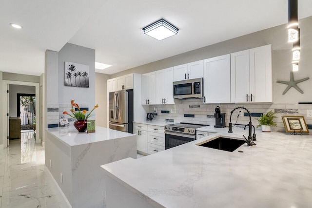 kitchen with kitchen peninsula, appliances with stainless steel finishes, tasteful backsplash, sink, and white cabinetry