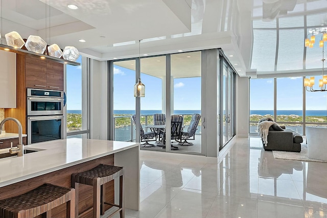 kitchen with floor to ceiling windows, stainless steel double oven, a notable chandelier, modern cabinets, and a raised ceiling