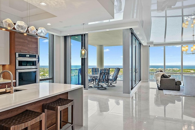 kitchen with stainless steel double oven, floor to ceiling windows, a raised ceiling, modern cabinets, and a chandelier