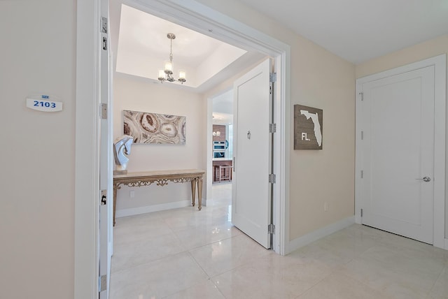 hallway featuring light tile patterned floors, baseboards, and a chandelier