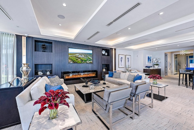 living area featuring recessed lighting, a glass covered fireplace, visible vents, and a tray ceiling