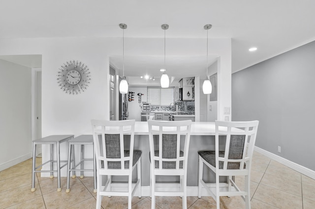 kitchen featuring backsplash, decorative light fixtures, light tile patterned flooring, and a breakfast bar area