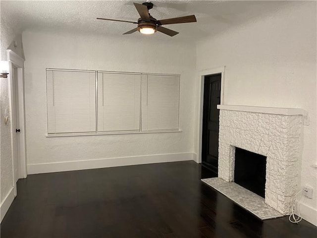 unfurnished living room with a textured ceiling, dark hardwood / wood-style floors, a stone fireplace, and ceiling fan