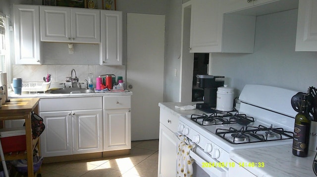 kitchen with white range with gas stovetop, light tile patterned flooring, white cabinetry, and sink