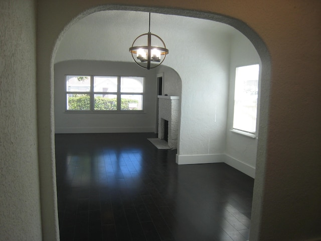 unfurnished living room featuring dark hardwood / wood-style floors, a fireplace, and an inviting chandelier