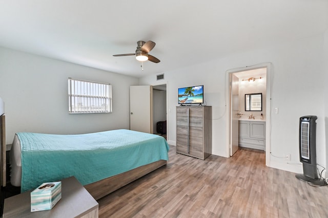 bedroom with light wood-type flooring, heating unit, ensuite bath, and ceiling fan