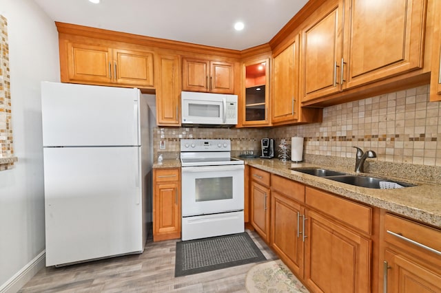 kitchen with tasteful backsplash, light stone counters, white appliances, sink, and light hardwood / wood-style flooring