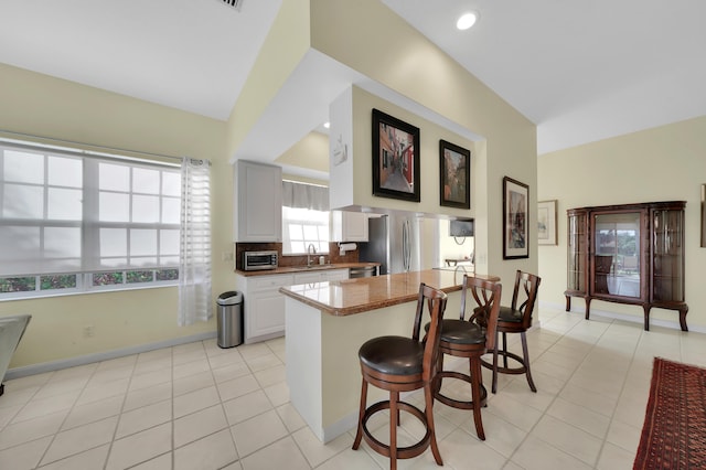 kitchen with a kitchen bar, kitchen peninsula, sink, white cabinets, and stainless steel refrigerator