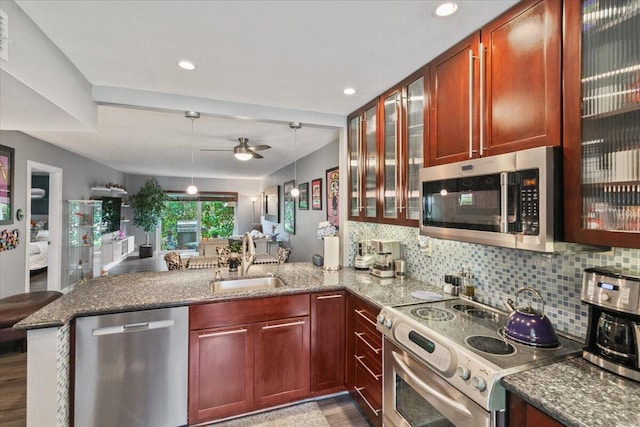 kitchen with sink, stainless steel appliances, kitchen peninsula, decorative light fixtures, and light wood-type flooring