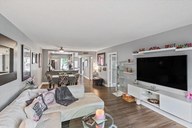 living room featuring wood-type flooring, a textured ceiling, and ceiling fan