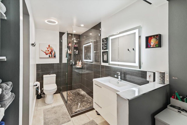 bathroom with vanity, a shower with door, tile patterned flooring, toilet, and tile walls