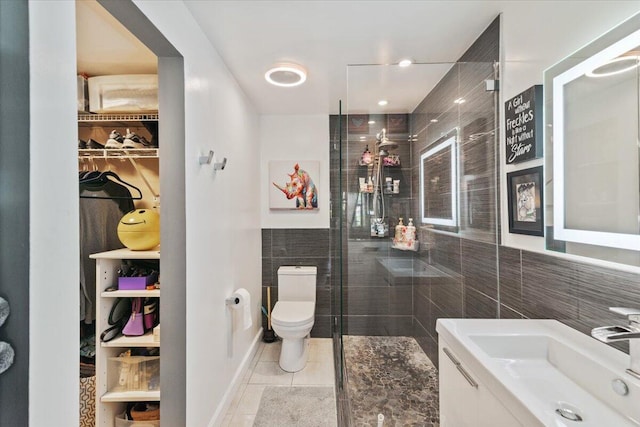 bathroom with tile patterned floors, a tile shower, vanity, tile walls, and toilet