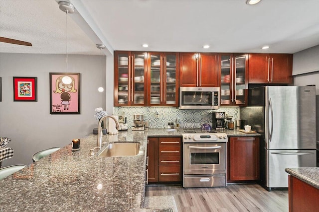 kitchen with sink, stainless steel appliances, dark stone counters, decorative light fixtures, and light wood-type flooring